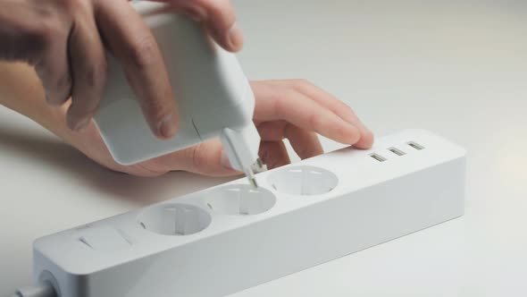 A Man Inserts a Large White Power Supply Into the Socket of a Modern Extension Cord Closeup alt