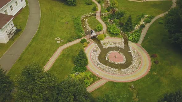 Newly Wedded Couple on Bridge Over Stream in Park Upper View alt
