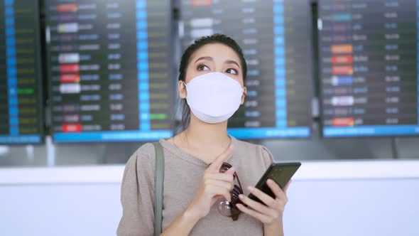 asian female traveller wearing face mask hand use smartphone checking map and flight schedule
