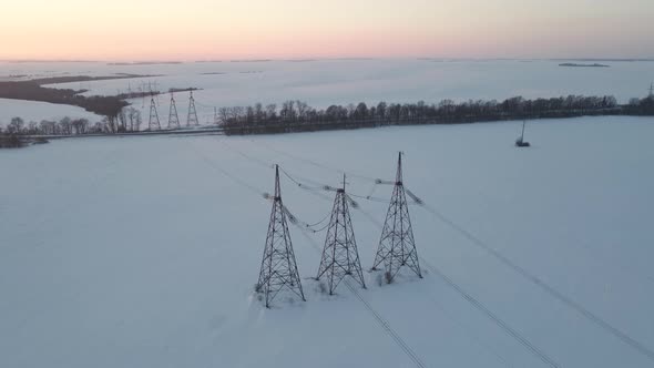 Aerial Drone View on Power Lines Over the Snowy Field at Sunset