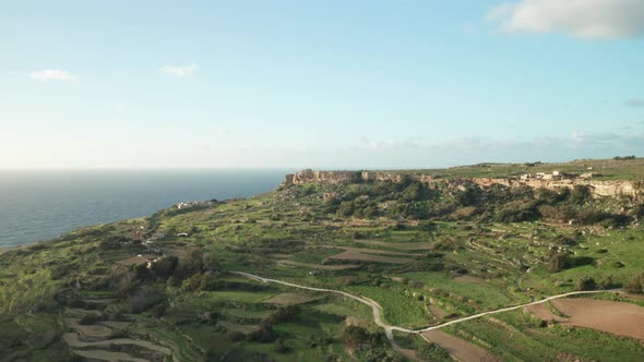 AERIAL: Rocky Cliffs near Green Paddy Fields in Malta on a Sunny Evening During Winter
