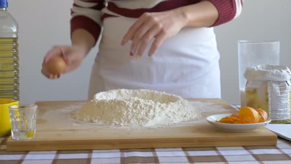 Woman adding egg to flour on baking board to make dough