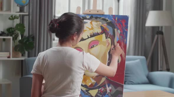 Hind View Of An Asian Artist Girl Holding Paintbrush Mixed Colour And Painting A Girl's Face alt