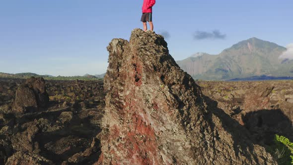 Man Wearing Red Jacket Standing on Mountain Peak in Rays of Evening Sun alt