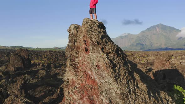 Man Wearing Red Jacket Standing on Mountain Peak in Rays of Evening Sun