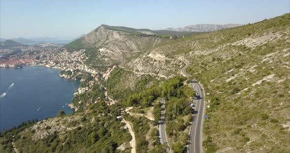 Aerial shot of Dubrovnik hills and roads with Old Town in the distance alt