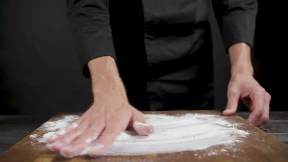 Cook Spreads Flour on Wooden Table on Black Background alt