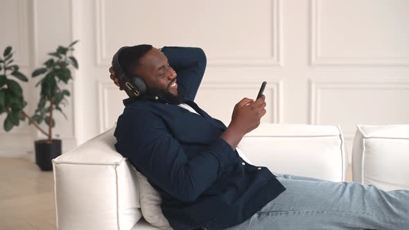 Satisfied African Guy is Enjoying Music Laying on Couch alt