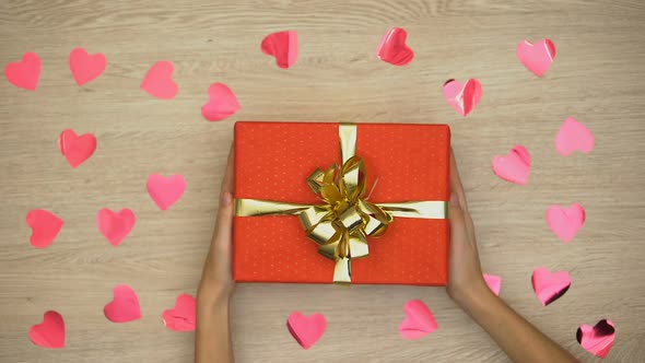 Lady Putting Present on Table Covered With Heart-Shaped Confetti, Top View alt