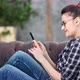 Smiling Hipster Young Woman Chatting Using Smartphone Sitting on Couch at Home Medium Shot