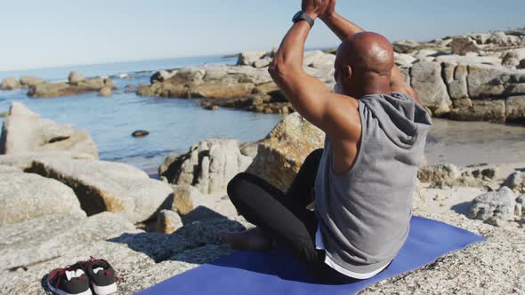 Senior african american man exercising stretching on rocks by the sea alt