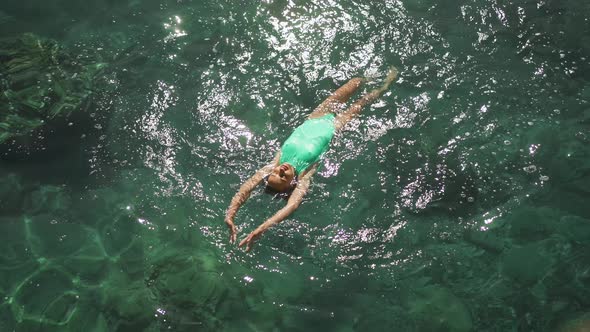 Slow Motion Top View of Sexy Beautiful Young Woman in Green Swimsuit Swimming on Back and Relaxing alt