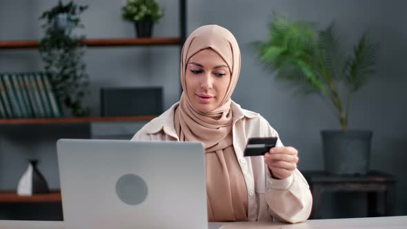 Smiling Muslim Woman Online Shopping Paying Card Black Friday Sale Discount Use Laptop at Home Desk alt