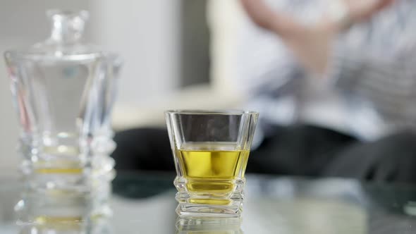 Closeup of Glass with Whiskey on Glass Table with Unrecognizable Blurred Man Crossing Hands No at alt