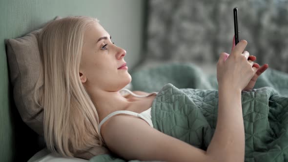 Face Closeup on Woman Typing a Message on a Mobile Phone Using 2 Hands While Comfortably Lying on a alt