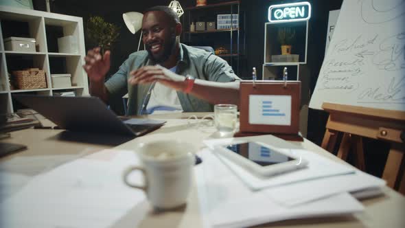 Smiling African Businessman Finishing Work in Coworking. Happy Afro Guy Relaxing alt
