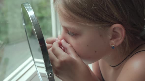 Young girl at home in front of mirror squeezes out pimples on her face.