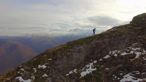 Aerial view of a trail runner running up the ridge of a snowy mountain. alt