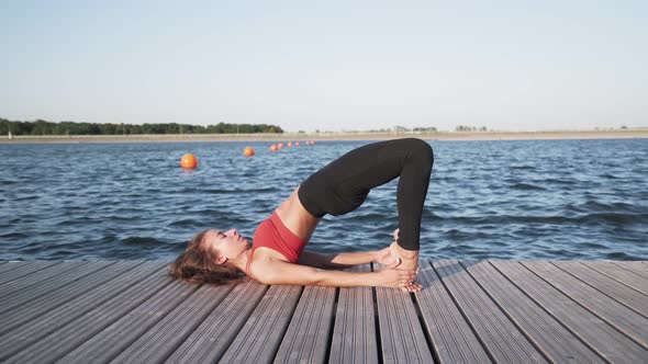 Young athletic Caucasian girl in a red tank top and leggings is doing stretching and yoga alt