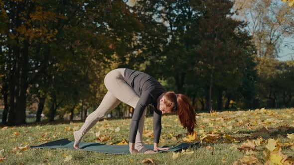 Young Woman Doing Revolved Side Angle Pose in Autumn City Park on a Yoga Mat