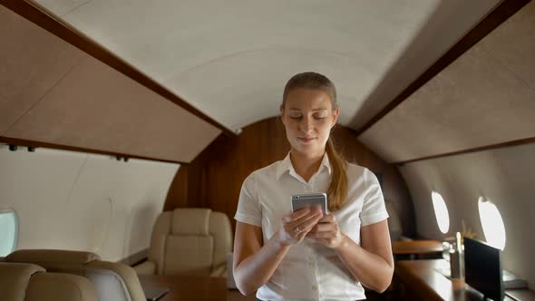 Busy Young Woman Typing Messages in Smartphone in Private Jet. alt