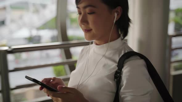 Portrait of asian woman with earphone listening music and using smartphone for chatting