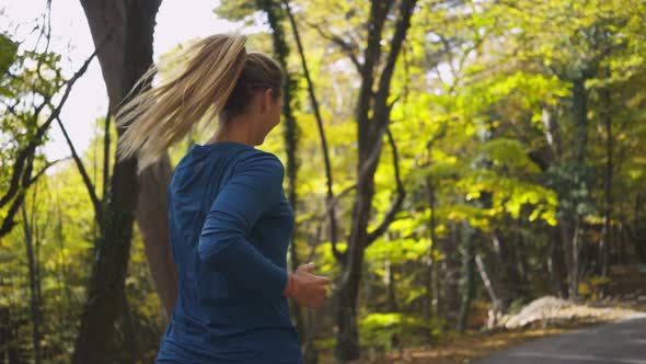 Cheerful Woman Runs Along Road in Autumn Forest and Jumps