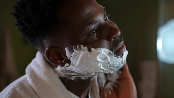 Closeup Side View Face of Concentrated African American Young Man Applying Shave Foam on Skin alt