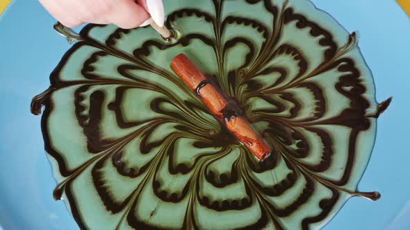 Close-up, a Pastry Chef Makes a Dessert Decoration, Draws with Chocolate on Caramel. Cinnamon Stick