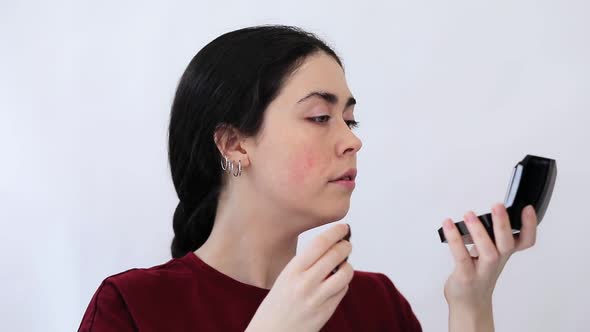 Portrait of a young woman masking redness on her cheeks with makeup. alt
