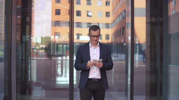 A Wealthy Businessman Counts Money Standing Near the Business Center Having a Good Mood alt
