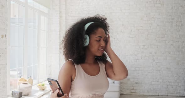 Young Trendy Woman in Big Headphones Listening Music and Dancing at Home alt