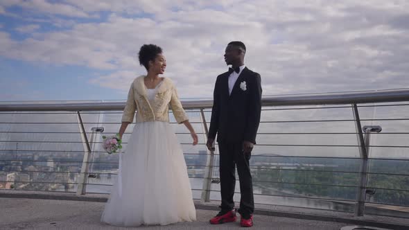 Cheerful African American Bride and Groom Jumping Up in Slow Motion on Bridge alt