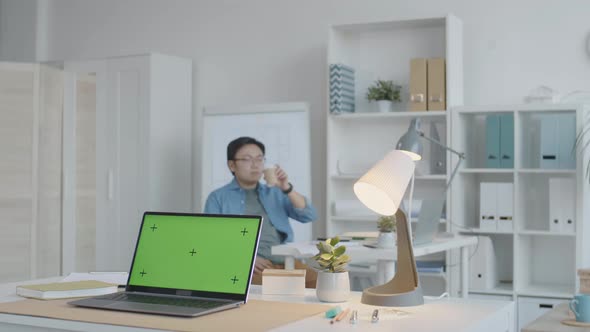 Man Drinking Tea and Using Smartphone in Office with Chroma Key Laptop alt