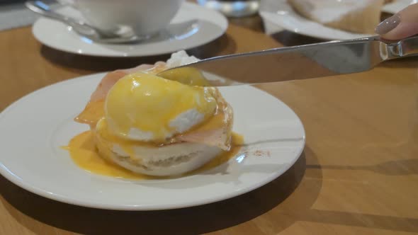 hand of woman cutting fresh egg benedict poached egg for breakfast alt
