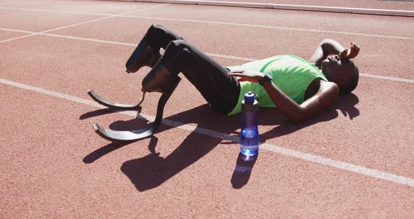 Disabled mixed race man with prosthetic legs lying on race track alt