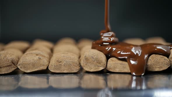 Thick Milk Chocolate is Poured Onto Brown Candies in a Row Lying on Culinary Foil alt