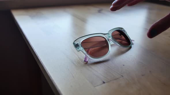 Cat-eye sunglasses are picked up off light wood table by a hand alt
