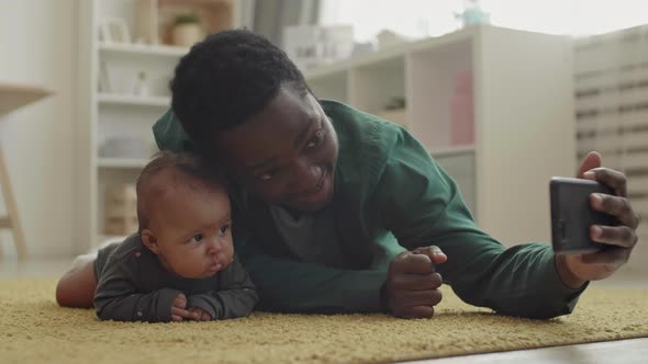 Father Lying on Carpet and Making Selfie with Baby alt