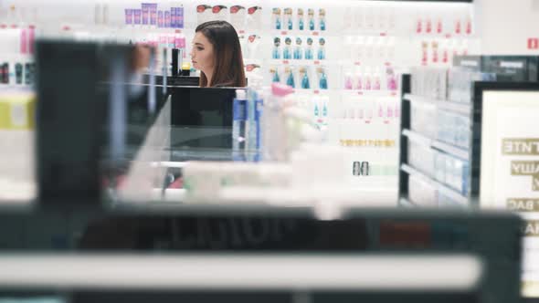Side View of Young Caucasian Woman Walks Past Stalls in Cosmetics Store alt