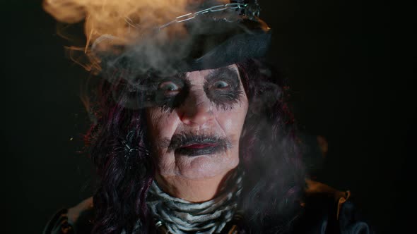 Creepy Mature Woman in Carnival Costume of Halloween Witch Blows Smoke From Mouth Trying to Scare alt