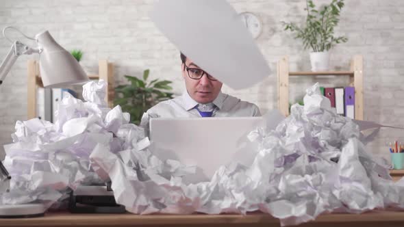 Male Office Worker Has a Lot of Work Sitting at a Laptop in a Heaps of Papers Slow Mo alt