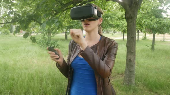 Young Woman In A Virtual Reality Helmet Uses A Virtual App In The Park alt