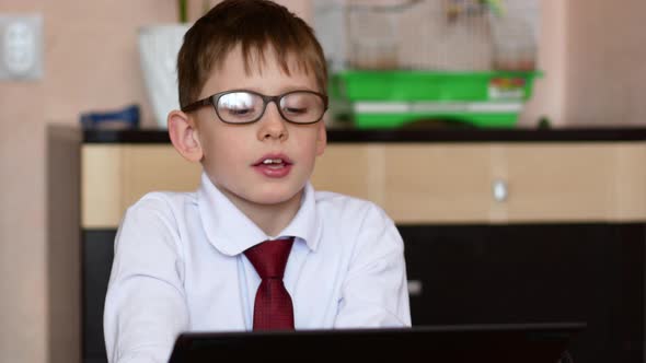 schoolboy in glasses sitting at home in front of a gadget participates in an online conference alt