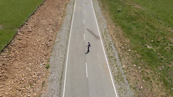 Guy in Summer in Black Clothes Descends From the Mountain on a Skateboard alt