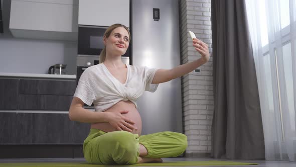 Young Caucasian Pregnant Woman Takes Pictures of Herself on Her Smartphone Poses Smiles