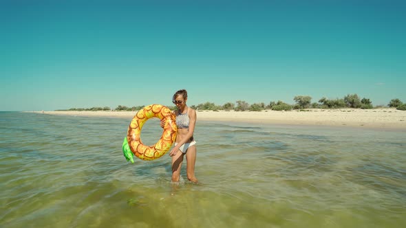 Portrait of Happy Smiling Young Woman in Sunglasses with Inflatable Pineapple Ring Walks in Sea alt