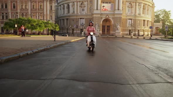 Young Beautiful Girl Riding Around City on Scooter at Sunrise alt