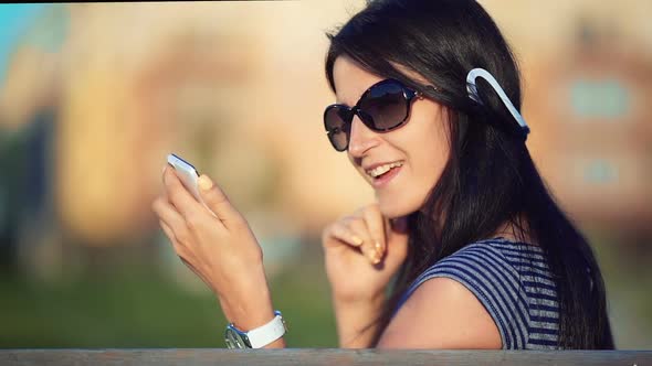 Young Brunette Straight Hair Woman in the Park Listening to Music with Headphones and Smartphone alt
