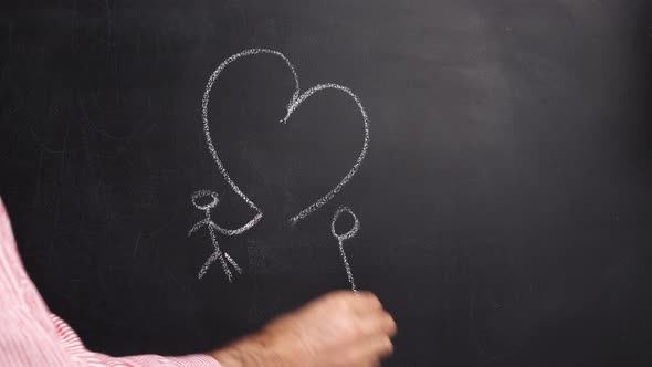 A man in a shirt draws white chalk on a black board two men united by one heart alt